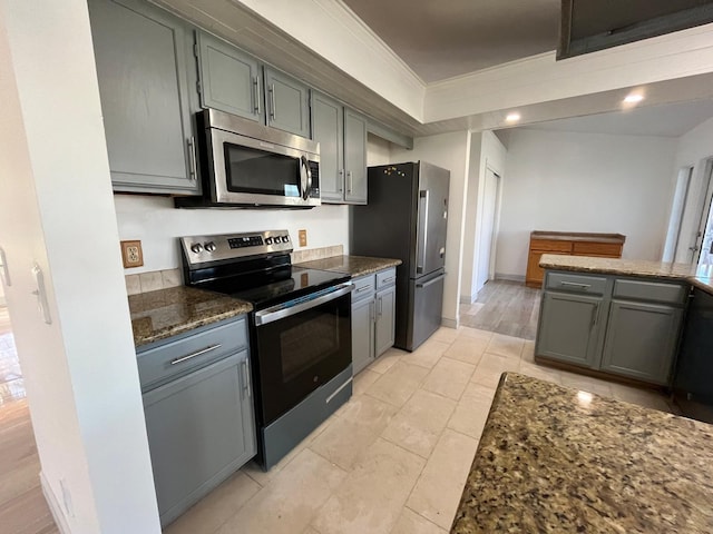 kitchen featuring gray cabinetry, crown molding, dark stone counters, light tile patterned floors, and appliances with stainless steel finishes