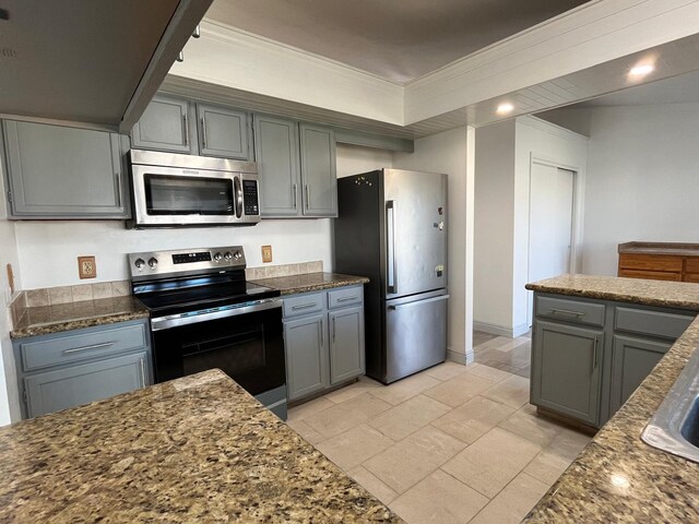 kitchen with gray cabinetry, ornamental molding, appliances with stainless steel finishes, and dark stone counters