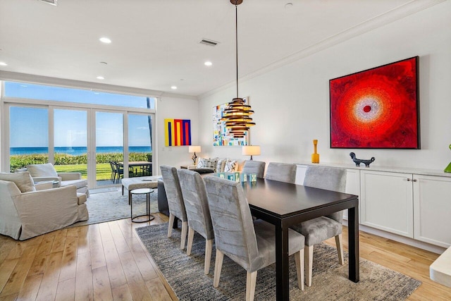 dining space featuring a water view, light wood-type flooring, and crown molding