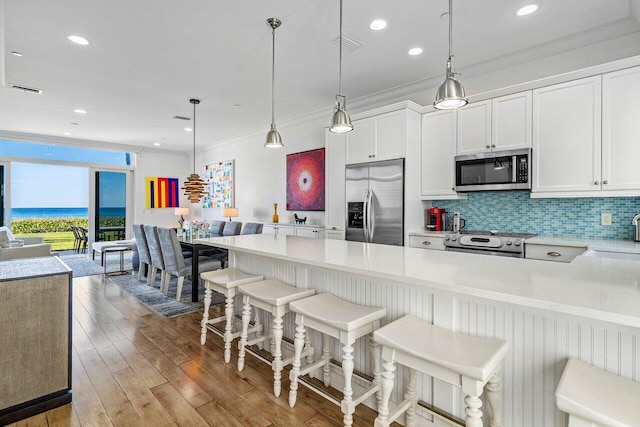 kitchen featuring pendant lighting, white cabinets, light wood-type flooring, a kitchen bar, and stainless steel appliances