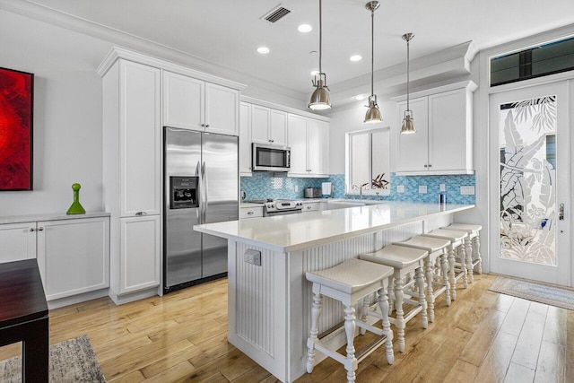 kitchen with pendant lighting, white cabinets, a kitchen breakfast bar, light wood-type flooring, and appliances with stainless steel finishes