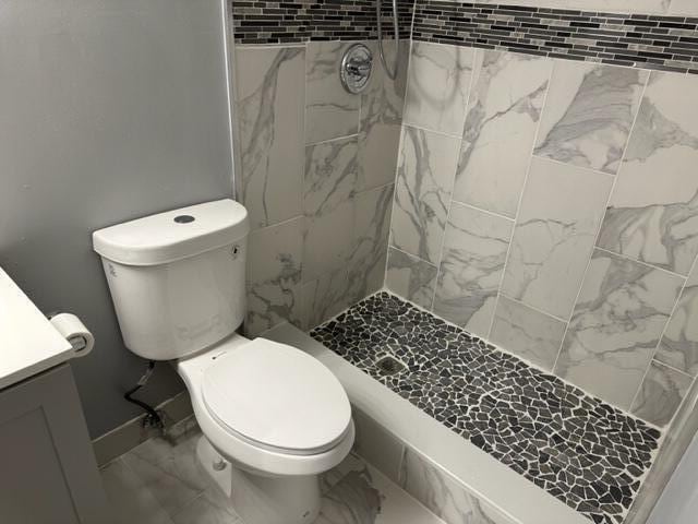 bathroom featuring toilet, vanity, and tiled shower