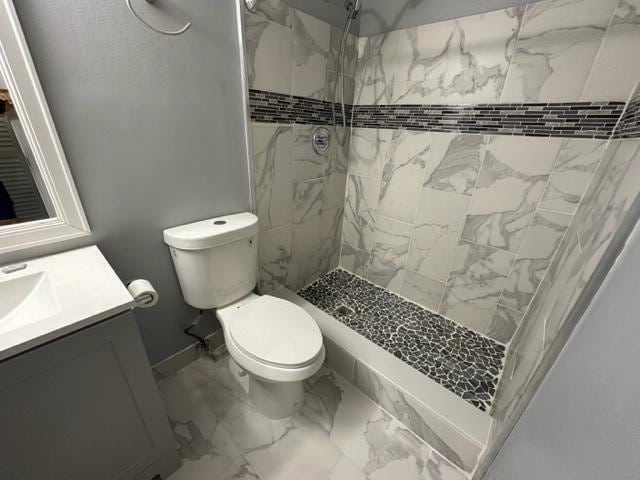 bathroom with a tile shower, vanity, and toilet