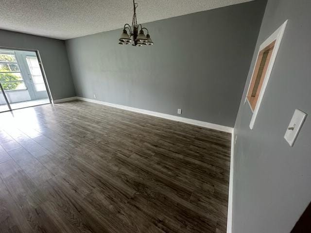 unfurnished room with dark wood-type flooring, a textured ceiling, and a notable chandelier