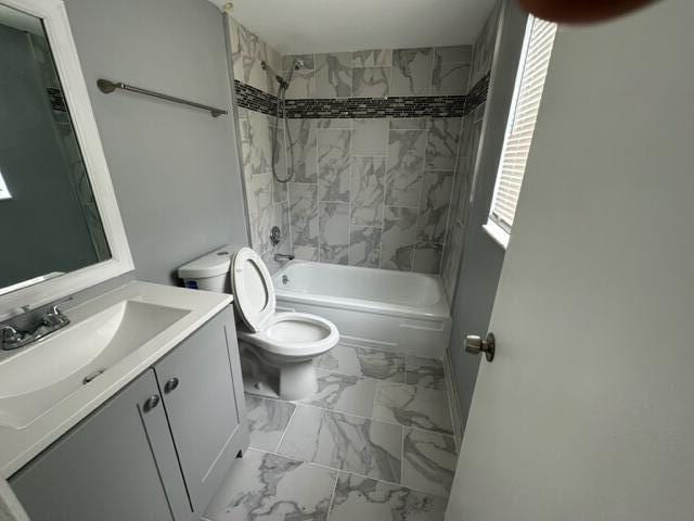 full bathroom featuring tiled shower / bath combo, toilet, and vanity