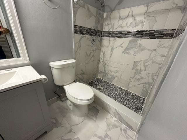 bathroom featuring a tile shower, vanity, and toilet