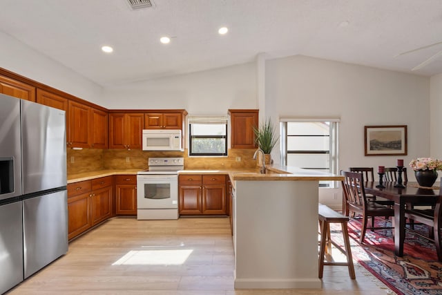 kitchen featuring sink, tasteful backsplash, white appliances, a kitchen bar, and light wood-type flooring