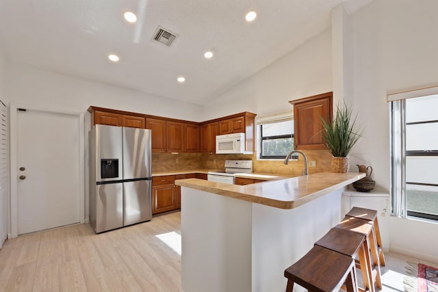 kitchen featuring high vaulted ceiling, kitchen peninsula, white appliances, a breakfast bar area, and light wood-type flooring