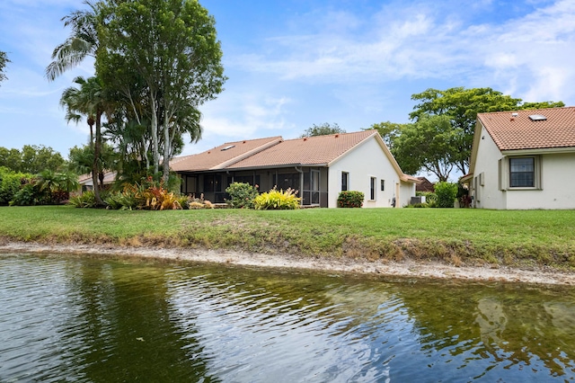 rear view of property featuring a water view, a lawn, and a sunroom