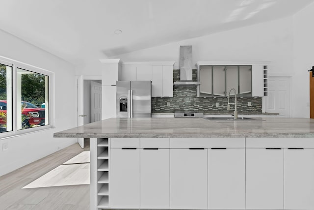 kitchen with light stone countertops, sink, wall chimney exhaust hood, stainless steel fridge with ice dispenser, and vaulted ceiling