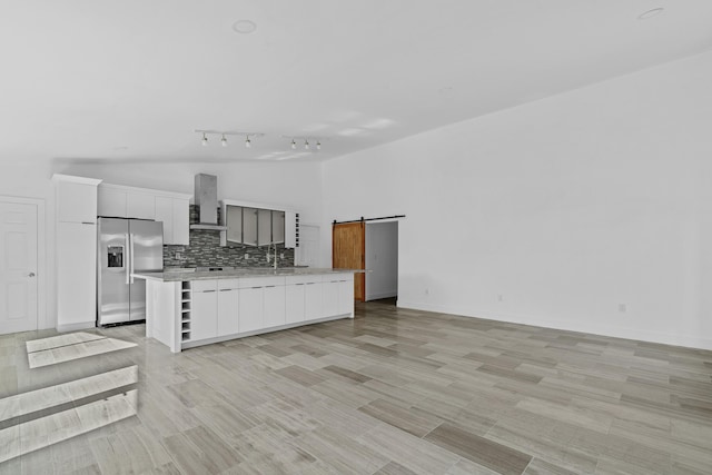 kitchen featuring stainless steel refrigerator with ice dispenser, a barn door, a kitchen island, and wall chimney exhaust hood