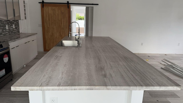 kitchen featuring decorative backsplash, light wood-type flooring, a breakfast bar, sink, and a barn door