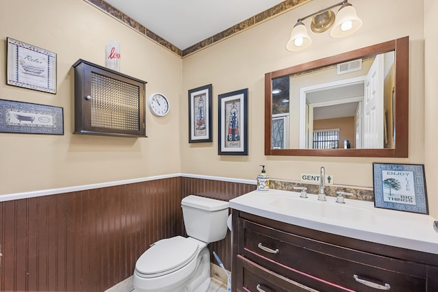 bathroom with a wainscoted wall, visible vents, vanity, and toilet