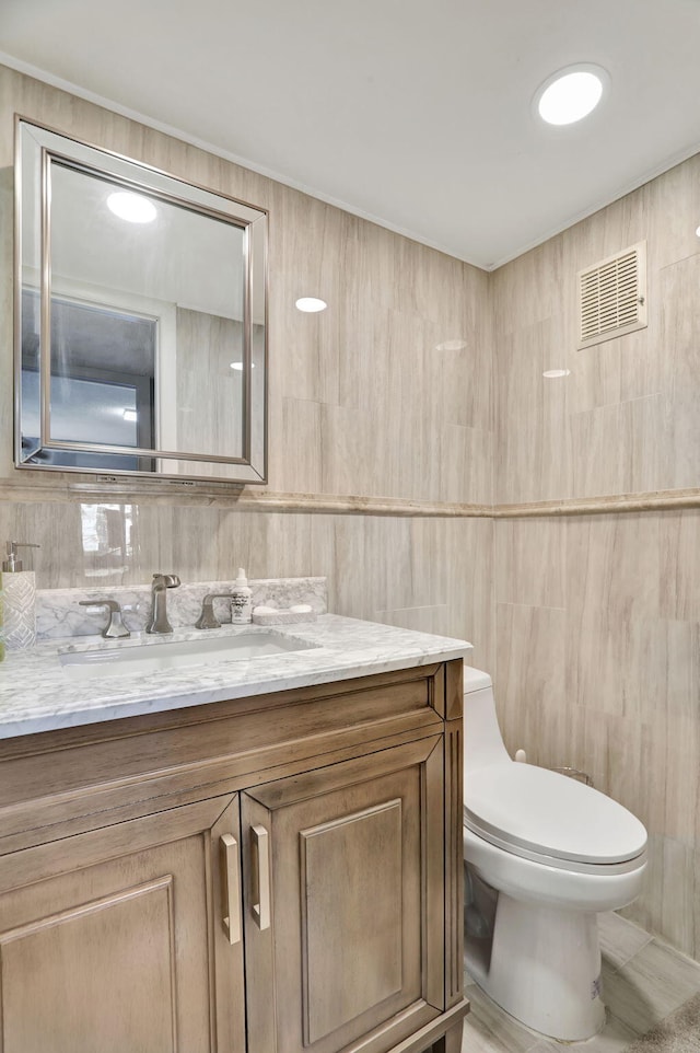 bathroom featuring toilet, tile walls, and vanity