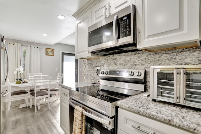 kitchen featuring white cabinetry, light hardwood / wood-style floors, stainless steel appliances, decorative backsplash, and light stone counters