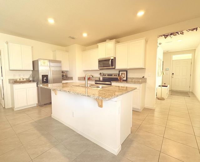 kitchen featuring sink, white cabinetry, light stone counters, appliances with stainless steel finishes, and a kitchen island with sink