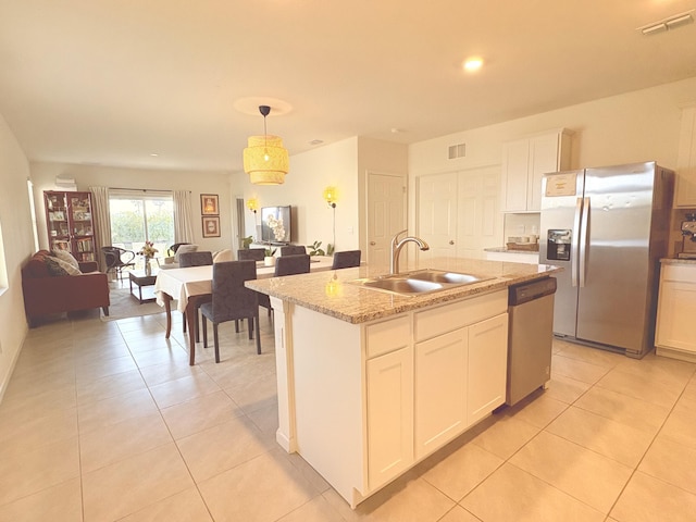 kitchen featuring sink, hanging light fixtures, stainless steel appliances, white cabinets, and a center island with sink