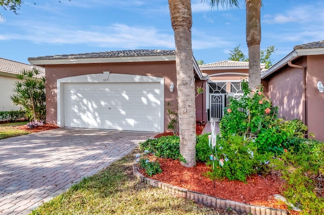 view of front of property with decorative driveway, an attached garage, a tile roof, and stucco siding