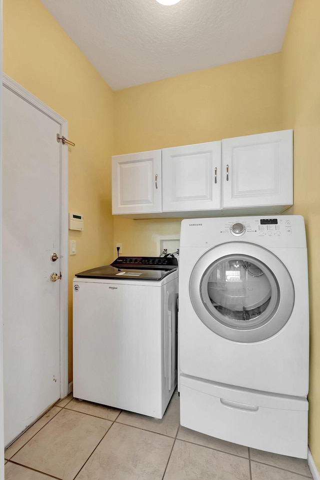 clothes washing area with a textured ceiling, cabinets, light tile patterned floors, and separate washer and dryer