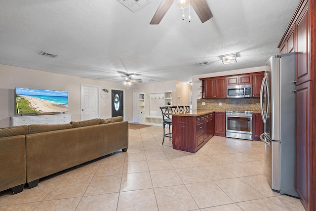 kitchen featuring backsplash, kitchen peninsula, a kitchen bar, light tile patterned floors, and appliances with stainless steel finishes