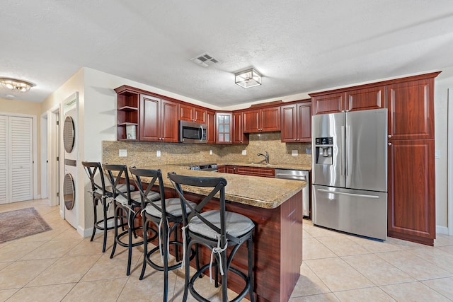 kitchen featuring backsplash, a textured ceiling, a kitchen bar, light tile patterned flooring, and appliances with stainless steel finishes