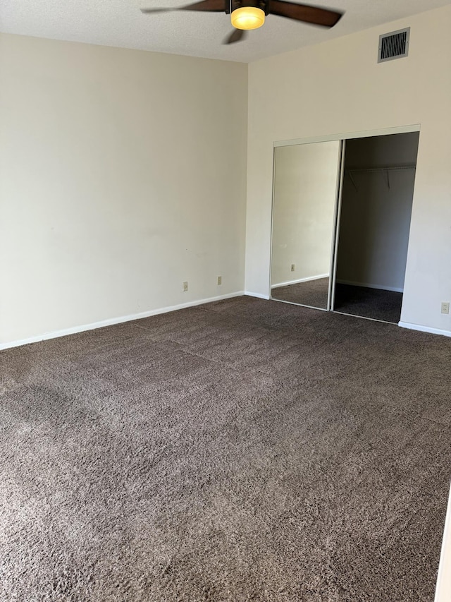 unfurnished bedroom featuring ceiling fan, a closet, and dark colored carpet