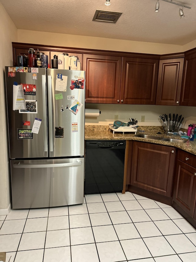 kitchen with dark stone counters, sink, dishwasher, stainless steel refrigerator, and light tile patterned flooring