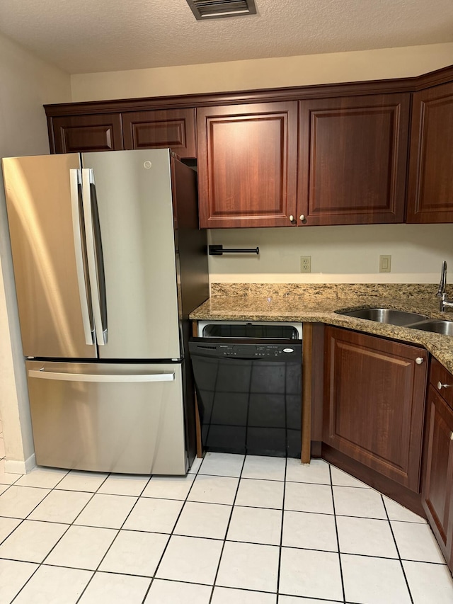 kitchen featuring dishwasher, sink, dark stone countertops, stainless steel fridge, and light tile patterned floors