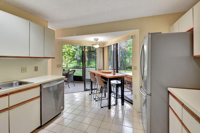 kitchen with appliances with stainless steel finishes, a textured ceiling, sink, light tile patterned floors, and white cabinetry