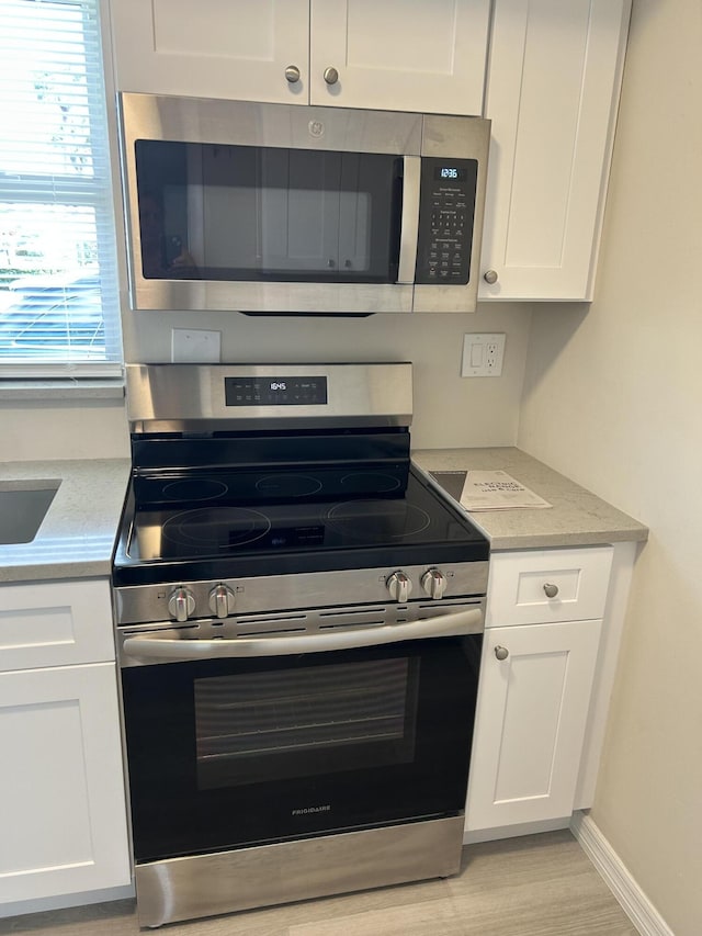 kitchen with light stone countertops, white cabinets, light hardwood / wood-style floors, and appliances with stainless steel finishes