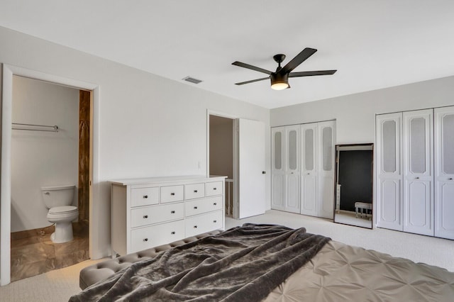 bedroom featuring ensuite bath, ceiling fan, light carpet, and multiple closets