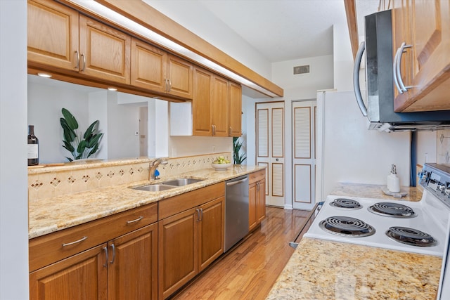 kitchen with light stone counters, sink, stainless steel appliances, and light hardwood / wood-style flooring