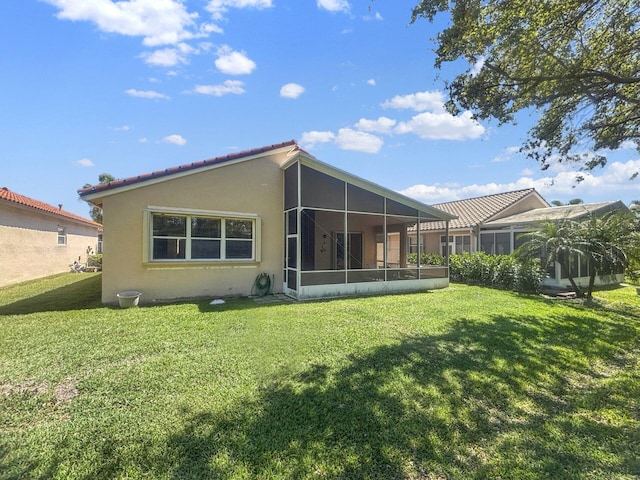 back of property with stucco siding, a lawn, a tiled roof, and a sunroom