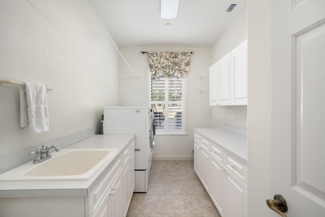 clothes washing area featuring washing machine and clothes dryer, sink, light tile patterned floors, and cabinets