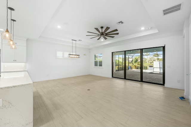 unfurnished living room with ceiling fan, a raised ceiling, and light hardwood / wood-style flooring