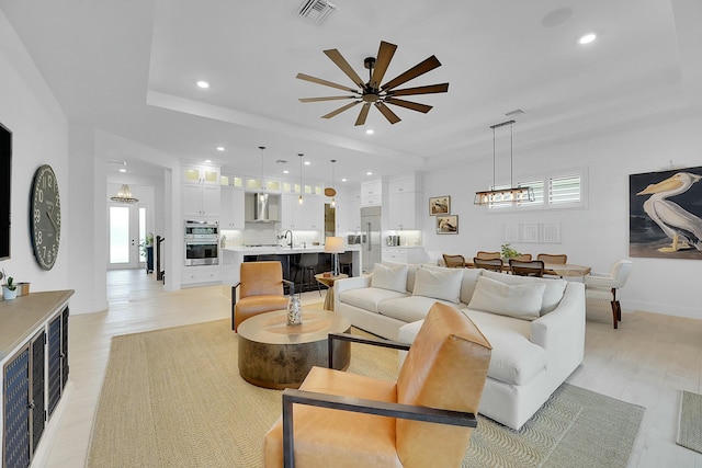 living room with a tray ceiling, plenty of natural light, sink, and light hardwood / wood-style flooring