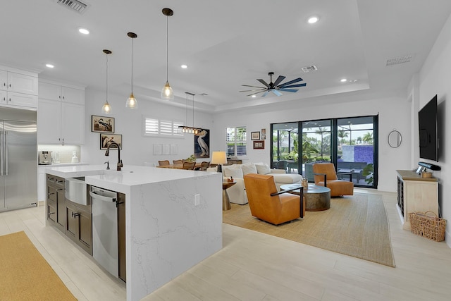 kitchen featuring white cabinetry, light stone counters, decorative light fixtures, a center island with sink, and stainless steel appliances