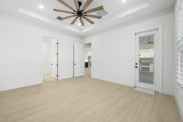 empty room with ceiling fan, a tray ceiling, and light hardwood / wood-style flooring