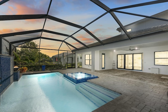 pool at dusk featuring an in ground hot tub, a patio, glass enclosure, and ceiling fan