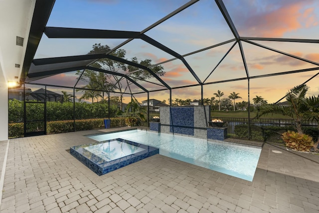 pool at dusk with a lanai, an in ground hot tub, and a patio