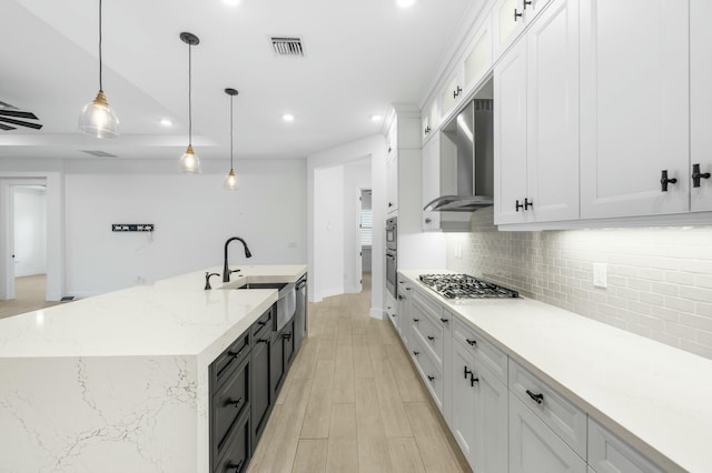 kitchen with white cabinetry, stainless steel appliances, ventilation hood, an island with sink, and pendant lighting