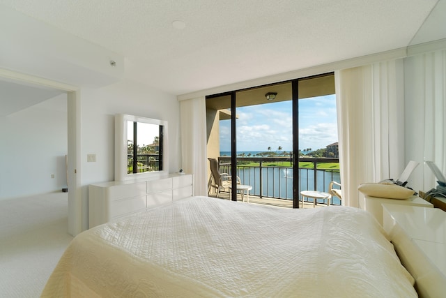 carpeted bedroom featuring expansive windows, a water view, a textured ceiling, and access to outside