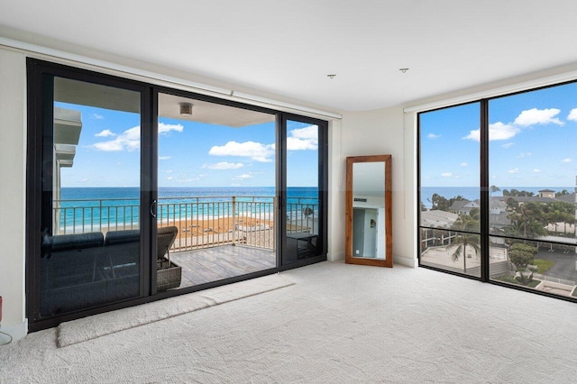 carpeted empty room with expansive windows, a water view, and a view of the beach