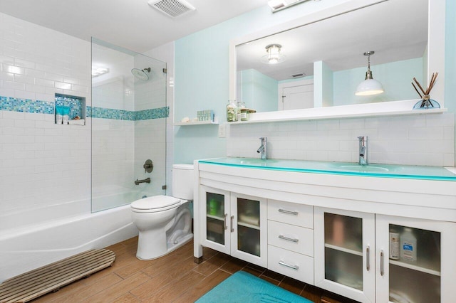 full bathroom with vanity, backsplash, tiled shower / bath combo, toilet, and wood-type flooring