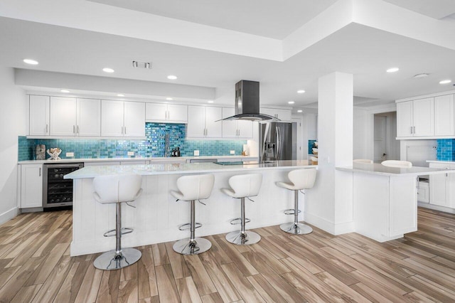 kitchen featuring stainless steel fridge, light wood-type flooring, island range hood, white cabinets, and wine cooler