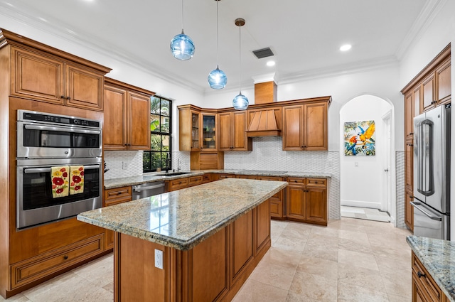 kitchen with crown molding, appliances with stainless steel finishes, a center island, light stone countertops, and decorative light fixtures