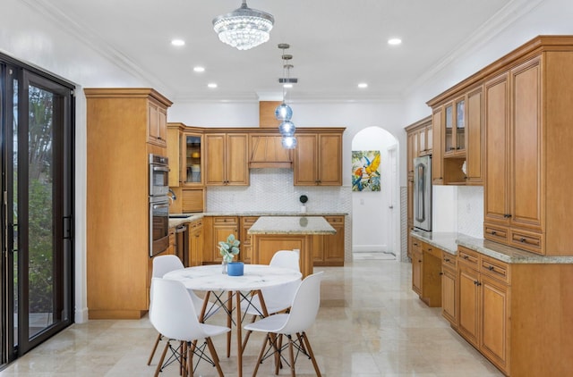 kitchen with tasteful backsplash, light stone counters, a kitchen island, decorative light fixtures, and ornamental molding