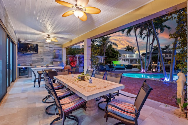 patio terrace at dusk featuring wine cooler, an outdoor kitchen, and ceiling fan