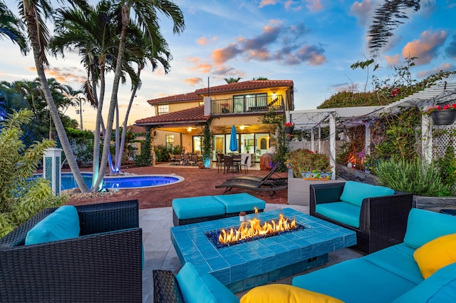 back house at dusk featuring a patio, a balcony, and an outdoor living space with a fire pit