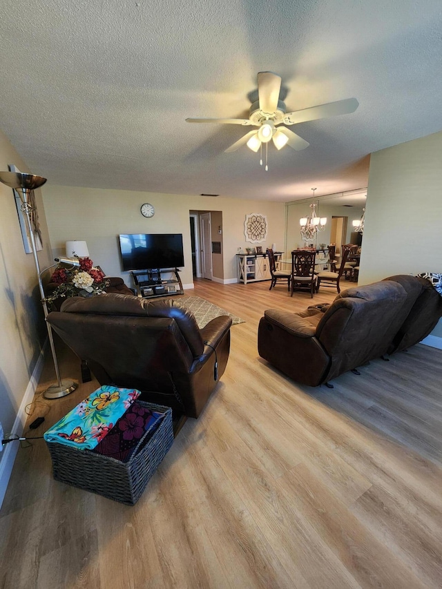 living room featuring a textured ceiling, ceiling fan with notable chandelier, and light hardwood / wood-style flooring